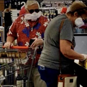 pareja pagando en un supermercado en la pandamia con unas compresas con alas a modo de mascarilla